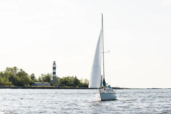 ホワイトスループは晴れた日にヨットを操縦しました 背景にある灯台と森 リガ湾 バルト海 ラトビア — ストック写真