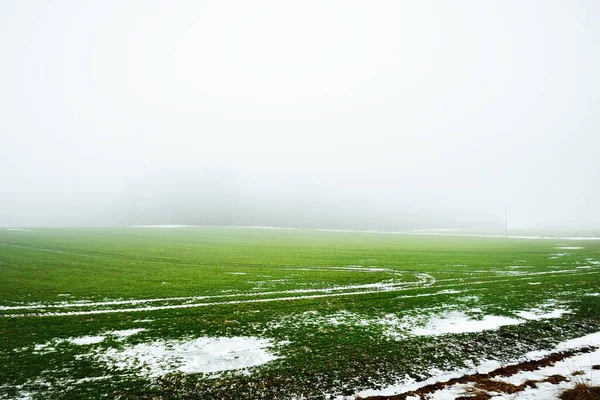 濃い霧の中で暗い空の下で緑の田園農業分野 地面に新鮮な雪 ポーランドの早春 コンセプトアート グラフィックミニマリズム エコロジー 地球温暖化 — ストック写真