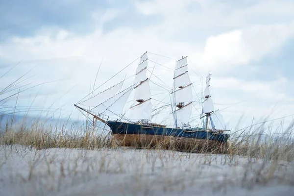 Antiquarian wooden scale model of the clipper tall ship, close-up. Dramatic sky, sandy shore (sand dunes) of the Baltic sea. Traditional craft, souvenir, toy, hobby, vintage, collecting, modeling