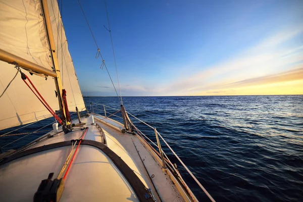 Sloop rigged yacht sailing at sunset. A view from the deck to the bow and sails. Waves and water splashes. Baltic sea, Latvia