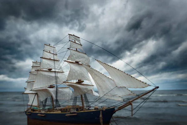 Antiquarian wooden scale model of the clipper tall ship, close-up. Dramatic sky, dark stormy clouds and sea. Traditional craft, souvenir, hobby, collecting, vintage, modeling. Zero waste concept