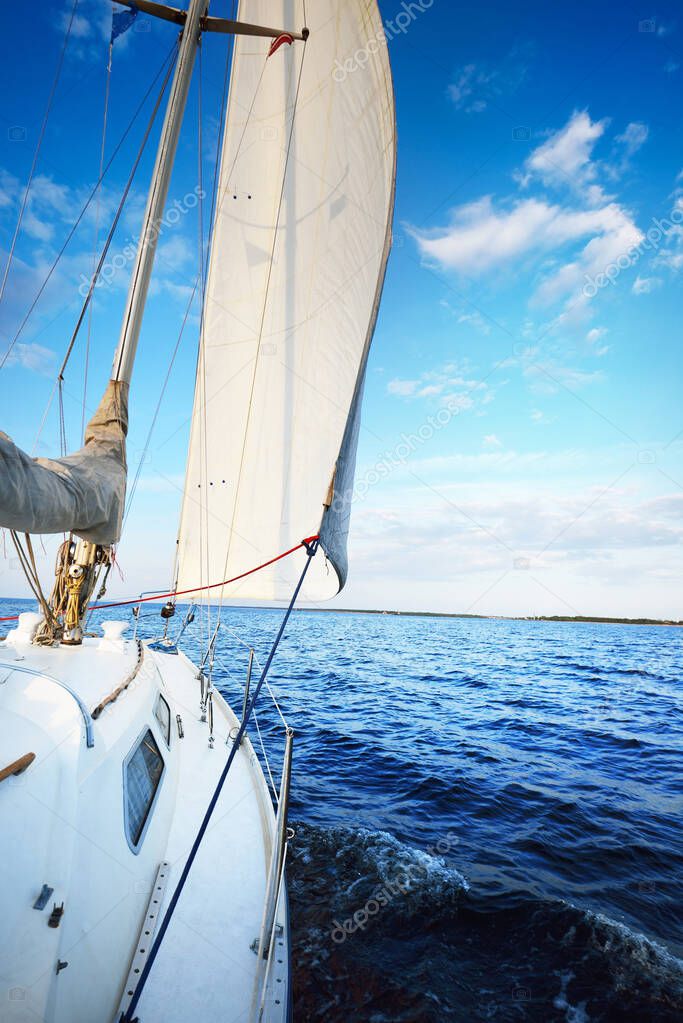 White yacht sailing in a still water at sunset. A view from the deck to the bow, mast and sails. Stunning cloudscape. Natural mirror. Sport and recreation theme. Baltic sea, Latvia