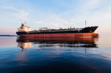 Gün batımında büyük bir kargo gemisi. Suyun yansıması. Renkli akşam bulutları ve parlak güneş ışığı. Baltık Denizi, Letonya