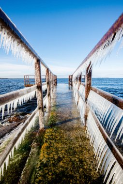 Güneşli bir günde, karla kaplı eski, paslı iskele. Buz parçaları yakın plan. Baltık Denizi, Letonya
