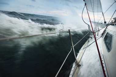 Fırtına sırasında bulutlu bir günde beyaz bir yat yelken açıyor. Güverteden pruvaya, direğe ve yelkenlere bir manzara. Dalgalar ve su sıçramaları. Finlandiya Körfezi