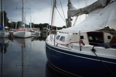 Mavi şalopalı yat iskeleye demirli, yakın plan. Fırtına gökyüzü. Suda yansıma. Riga Limanı, Letonya
