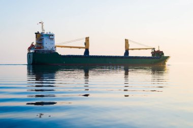 Gün batımında büyük bir yük vinci gemisi. Akşam bulutları ve parlak güneş ışığı. Baltık Denizi, Letonya