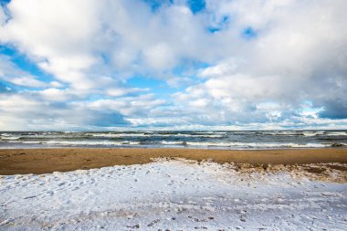 Güneşli bir kış gününde, karla kaplı deniz kıyısında. Kuzey denizi üzerinde soğuk fırtınalı dalgalar ve bulutlar, Hollanda