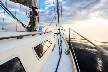 Gün batımında durgun suda yüzen beyaz bir yat. Güverteden pruvaya, direğe ve yelkenlere bir manzara. Şaşırtıcı bulut manzarası. Doğal ayna. Spor ve eğlence teması. Baltık Denizi, Letonya