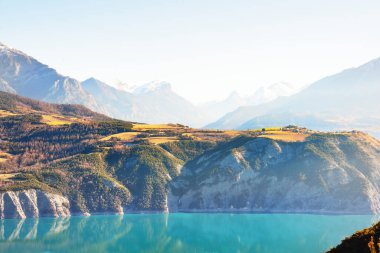 Güneşli bir günde Fransız Alplerindeki dağ gölü Lac de Serre-poncon 'un panoramik manzarası. Açık mavi gökyüzü, durgun su. Seyahat yerleri, turizm, dönüm noktası, doğa, Fransa 'da Noel tatilleri