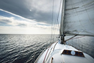 ABD 'nin güneybatı limanında, Maine kıyısında beyaz yelkenli yelkenli yelkenli. Güverteden pruvaya, direğe ve yelkenlere bir manzara. Koyu mavi fırtına gökyüzü, güneş bulutların arasından ışıldıyor
