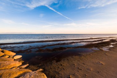 Gün batımında Rocky sahili. Açık mavi gökyüzü, beyaz bulutlar ve uçak izleri. Baltık Denizi, Ruhnu Adası, Estonya