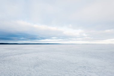 Kış manzarası. Gün batımında donmuş karla kaplı göl manzarası. Arka planda orman var. Renkli akşam bulutları. Onega Gölü, Karelia, Rusya