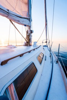 Sakin su. Günbatımında beyaz yelkenli tekneyle denize açılacak. Güverteden pruvaya, direğe ve yelkenlere bir manzara. Baltık Denizi, Letonya