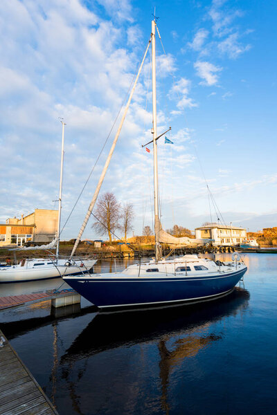 Blue sloop rigged yacht moored to a pier after winterization in winter. Clear blue sky. Port of Riga, Latvia