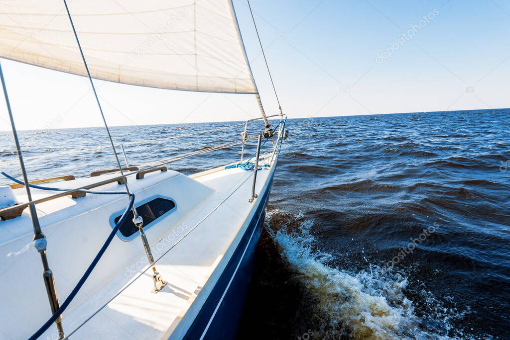 White yacht sailing in an open Baltic sea on a clear day. A view from the deck to the bow and sails. Waves and water splashes. Latvia