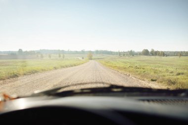 Açık bir günde tarlalardan geçen köy yolu. Sıcak gün ortası güneşi, açık gökyüzü. Arabadan bir manzara. Seyahat yerleri, tatiller, özgürlük, sürüş, ulaşım