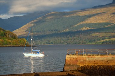 Loch Fyne yakınlarındaki sahil, orman ve tepelerin manzarası. Beyaz yelkenli yatla yakın plan. Inveraray, Inner Hebrides, Argyll ve Bute, İskoçya, İngiltere