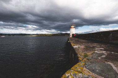 Eski deniz fenerine doğru boş bir gezinti, yakın plan. Arka planda kayalık kıyılar var. Dramatik bulut manzarası. Ardrishaig, Crinan Kanalı, İskoçya, İngiltere. Seyahat yerleri, gezi teması