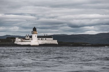 Jura adasının batı kıyısının kayalık kıyıları, yatın manzarası. Beyaz deniz feneri yakın plan. Fırtınadan sonra dramatik bulutlar. Inner Hebrides, İskoçya, İngiltere. Atmosferik manzara