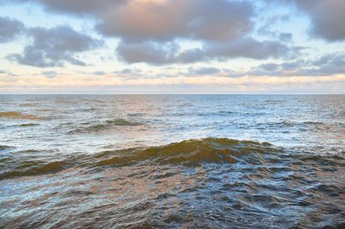 Gün batımında açık Baltık denizinin panoramik görüntüsü. Renkli parlak kümülüs bulutlarıyla dramatik bir gökyüzü. Su yüzeyi dokusu yakın çekim. Dengesiz hava, kış, iklim değişikliği, okyanus kabarması, doğa.