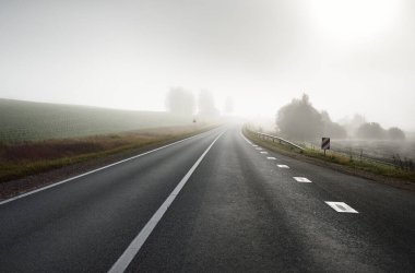 Gün doğumunda sisli bir havada boş otobanın arabasından ormana ve tarlalara doğru panoramik bir manzara. Avrupa. Ulaşım, lojistik, seyahat, yolculuk, özgürlük, sürüş. Kırsal alan