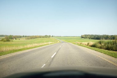 Açık bir günde tarla ve orman boyunca asfalt yol (karayolu). Sıcak gün ortası güneşi, açık gökyüzü. Arabadan bir manzara. Seyahat yerleri, tatiller, özgürlük, sürüş, ulaşım