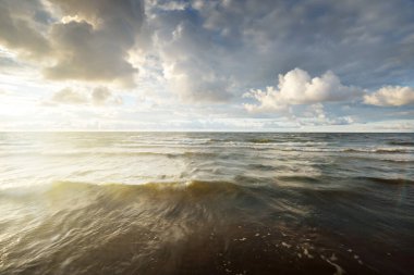 Gün batımında fırtınadan sonra Baltık kıyıları üzerinde parlayan kümülüs bulutlarıyla açık bir gökyüzü. Dramatik bulut manzarası. Sıcak altın güneş ışığı. Resimli bir manzara var. Hava kararsız. Uzun pozlama