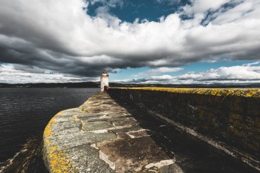 Eski deniz fenerine doğru boş bir gezinti, yakın plan. Arka planda kayalık kıyılar var. Dramatik bulut manzarası. Ardrishaig, Crinan Kanalı, İskoçya, İngiltere. Seyahat yerleri, gezi teması