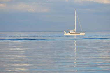 Beyaz modern yat (katamaran) gün batımında açık bir Karayip denizinde yüzüyor. Açık mavi gökyüzü, suda simetri yansımaları. Idyllic deniz manzarası. Seyahat yerleri, spor, boş zaman aktivitesi, dinlenme