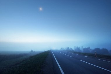 Gece sisli bir havada boş otobanın panoramik görüntüsü. Ay ışığı, temiz gökyüzü. Gün doğumu. Avrupa. Ulaşım, lojistik, seyahat, yolculuk, özgürlük, sürüş. Kırsal alan