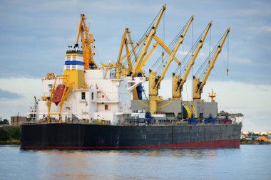 Gün batımında limana demir atmış büyük bir kargo gemisi. Vinçler arka planda. Riga, Baltık Denizi, Letonya. Yük taşımacılığı, küresel iletişim, lojistik, çevresel hasar