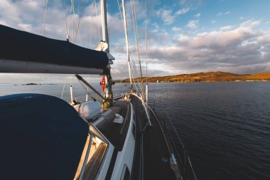 Günbatımında Islay Adası kıyısında seyir halindeki ahşap meşe güvertesiyle donatılmış modern bir yat. Inner Hebrides, İskoçya, İngiltere. Spor ve eğlence, seyahat yerleri, dönüm noktaları, ulaşım