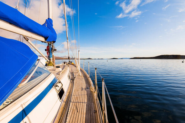 Sloop rigged modern yacht with wooden teak deck sailing near the rocky shore of Jura island at sunset, close-up. Inner Hebrides, Scotland, UK. Sport, recreation, cruise, travel destinations