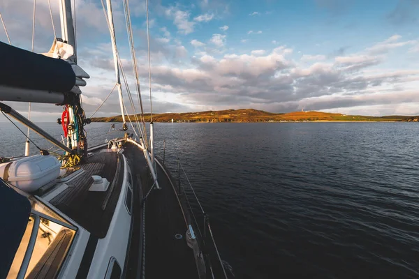 Sloop rigged modern yacht with wooden teak deck sailing near the shore of Isle of Islay at sunset. Inner Hebrides, Scotland, UK. Sport and recreation, travel destinations, landmarks, transportation