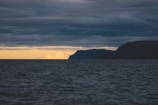 Sailing near the rocky shores (cliffs) of the west coast of Jura island, a view from the yacht. Dramatic sunset sky with glowing clouds. Inner Hebrides, Scotland, UK. Travel destinations, landmarks