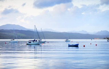 Göz kamaştırıcı gün batımı bulutları. Küçük bir köy olan Rhu, İskoçya, İngiltere kıyısında demirli yelkenliler ve ahşap botlar.