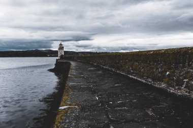 Eski deniz fenerine doğru boş bir gezinti, yakın plan. Arka planda kayalık kıyılar var. Dramatik bulut manzarası. Ardrishaig, Crinan Kanalı, İskoçya, İngiltere. Seyahat yerleri, gezi teması