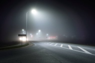 Aydınlatılmış yeni otoyolun panoramik manzarası gece sisli, sokak ışıkları yakın. Ay ışığı. Karanlık şehir manzarası. Avrupa. Ulaşım, lojistik, seyahat, turizm, yol gezisi, özgürlük, sürüş