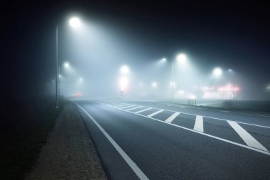 Aydınlatılmış yeni otoyolun panoramik manzarası gece sisli, sokak ışıkları yakın. Ay ışığı. Karanlık şehir manzarası. Avrupa. Ulaşım, lojistik, seyahat, turizm, yol gezisi, özgürlük, sürüş