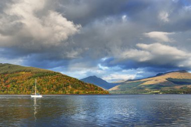 Loch Fyne yakınlarındaki sahil, orman ve tepelerin manzarası. Beyaz yelkenli yatla yakın plan. Inveraray, Inner Hebrides, Argyll ve Bute, İskoçya, İngiltere