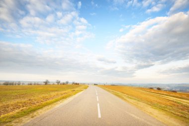 Tarlalarda boş bir asfalt yol (karayolu). Dramatik bir gökyüzü. Fransa, Avrupa. Ulaşım, lojistik, seyahat merkezleri, turizm, sürüş, hız, özgürlük, tecrit