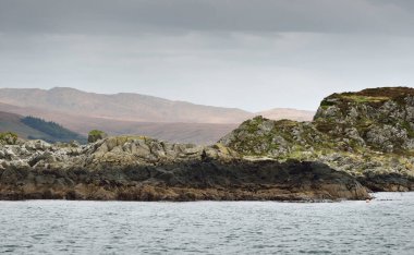 Jura adasının kıyılarının panoramik manzarası, dağları ve vadileri sudan. Bulutlu mavi gökyüzü. Fırtınalı hava. Paps of Jura, Inner Hebrides, İskoçya, İngiltere