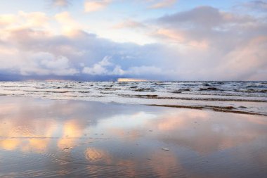 Kumlu bir sahilden Baltık Denizi 'nin panoramik manzarası. Açık günbatımı gökyüzü, parlak pembe bulutlar, yumuşak ışık. Suyun simetri yansımaları, doğal ayna. Hava, kış, iklim değişikliği, doğa