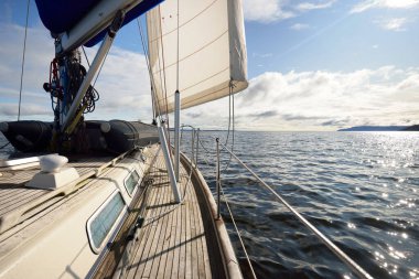 Bulutlu bir günde ahşap meşe güverteli, yelkenli, modern bir yat. Direğe ve yelkenlere bir manzara. Su, yakından sıçrıyor. Tarbert, İskoçya, İngiltere