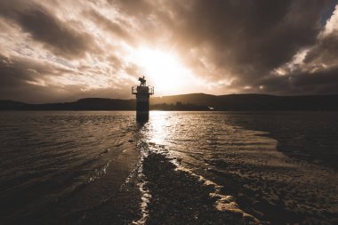 Yağmurdan sonra karanlık fırtınalı gökyüzünün altında Rocky gölü kıyıları ve deniz feneri. Dramatik bulut manzarası. Gare Loch, Rhu, İskoçya, İngiltere. Seyahat yerleri, tatiller, boş zaman aktivite kavramları