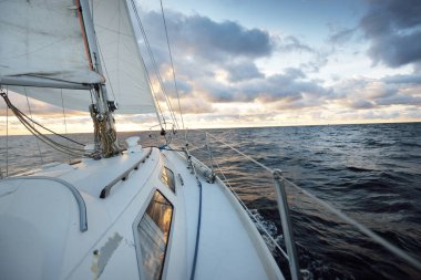Gün batımında açık denizde yelken açmak. Güvertenin yakın görüntüsü, direk ve yelkenler. Yağmurdan sonra açık gökyüzü, çarpıcı parlayan bulutlar, altın güneş ışığı, dalgalar ve su sıçramaları, kasırga. Destansı deniz manzarası