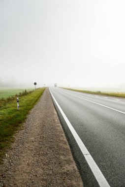 Gün doğumunda sisli bir havada boş otobanın arabasından ormana ve tarlalara doğru panoramik bir manzara. Avrupa. Ulaşım, lojistik, seyahat, yolculuk, özgürlük, sürüş. Kırsal alan