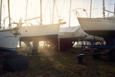 Kışlık şalopa donanımlı yat karada duruyor, yakın plan. Yeni yelken sezonunu bekliyorum. Gün batımında yat kulübü (marina). Yumuşak akşam ışığı. Denizcilik gemisi, servis, ulaşım