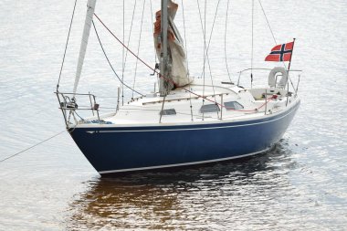 Kumlu kıyıya yakın sığ sularda demirli mavi şalopeli bir yat. Yakın çekim görüntüsü. Boş zaman aktivitesi, spor, eğlence teması. Glomma Nehri, Oslofjord, Norveç